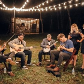 Bluegrass musicians sitting outside of a barn playing their instruments