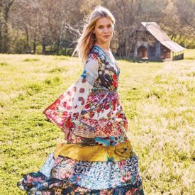 Woman in colorful dress posed in the grass in front of an old barn