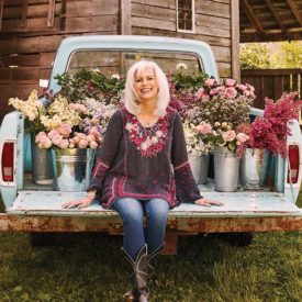 Woman sitting on the bed of an old pickup truck with flowers